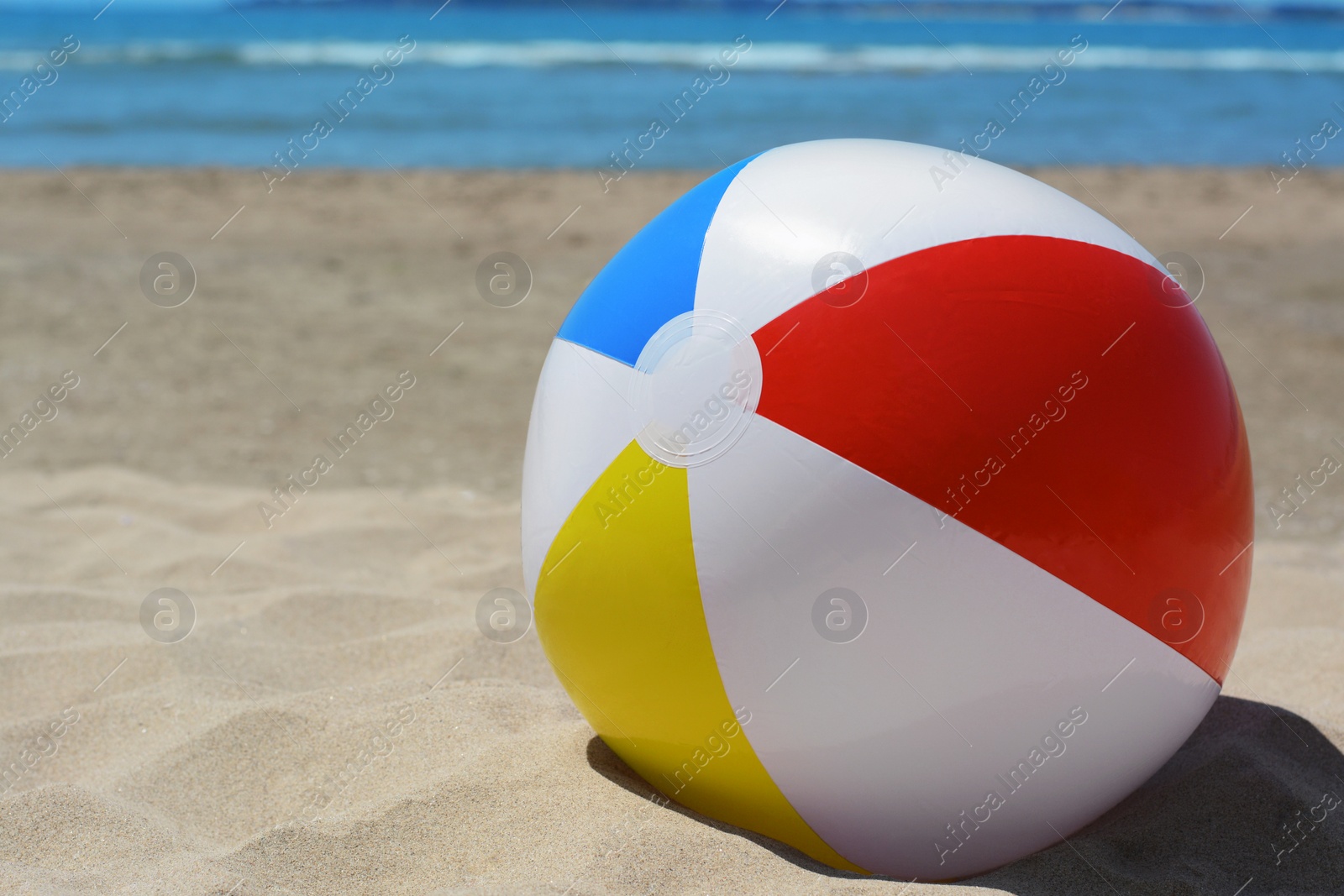 Photo of Colorful beach ball on sand near sea, space for text