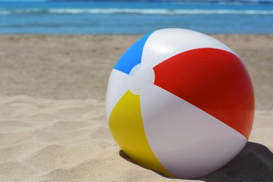 Colorful beach ball on sand near sea, space for text