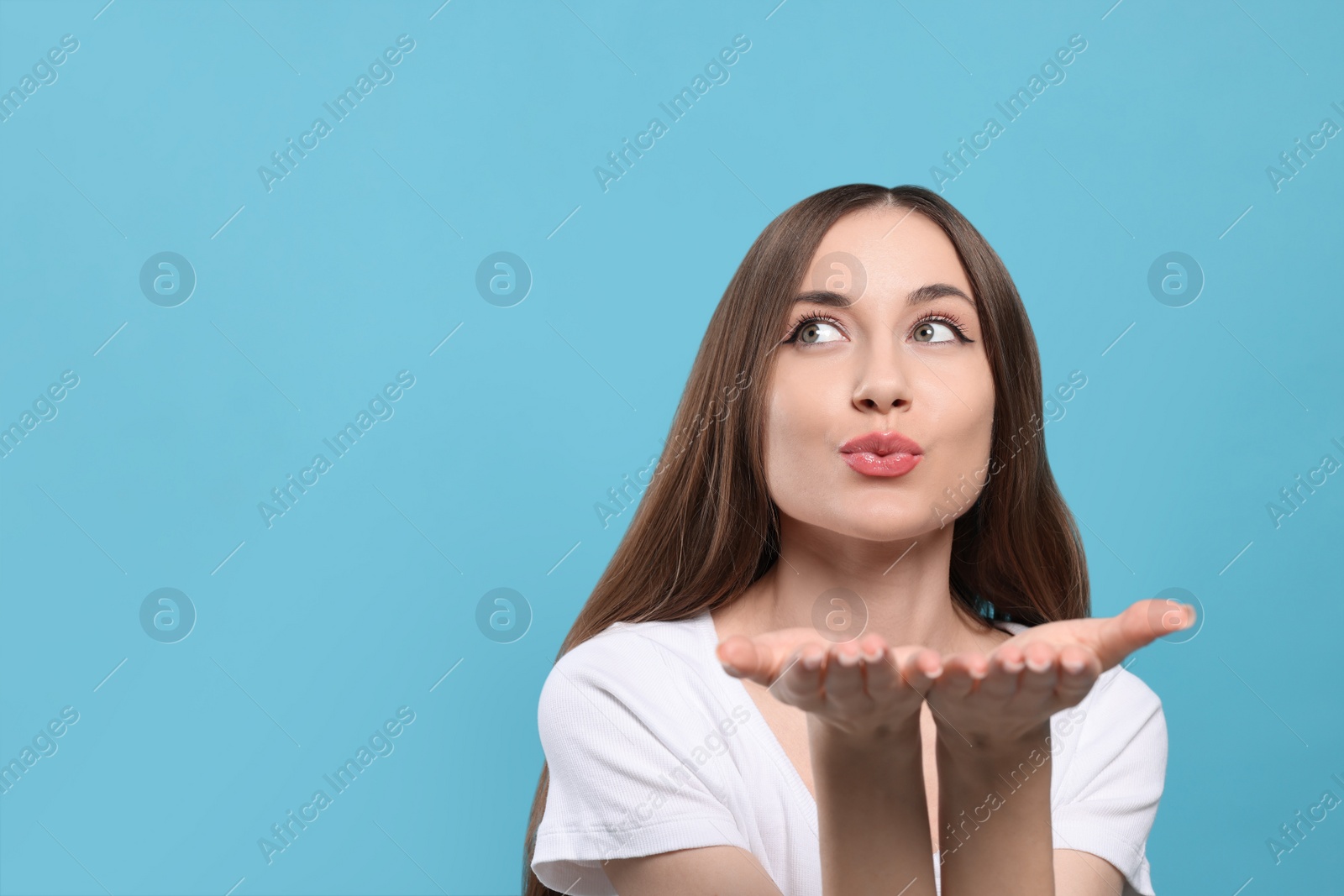 Photo of Beautiful young woman blowing kiss on light blue background, space for text