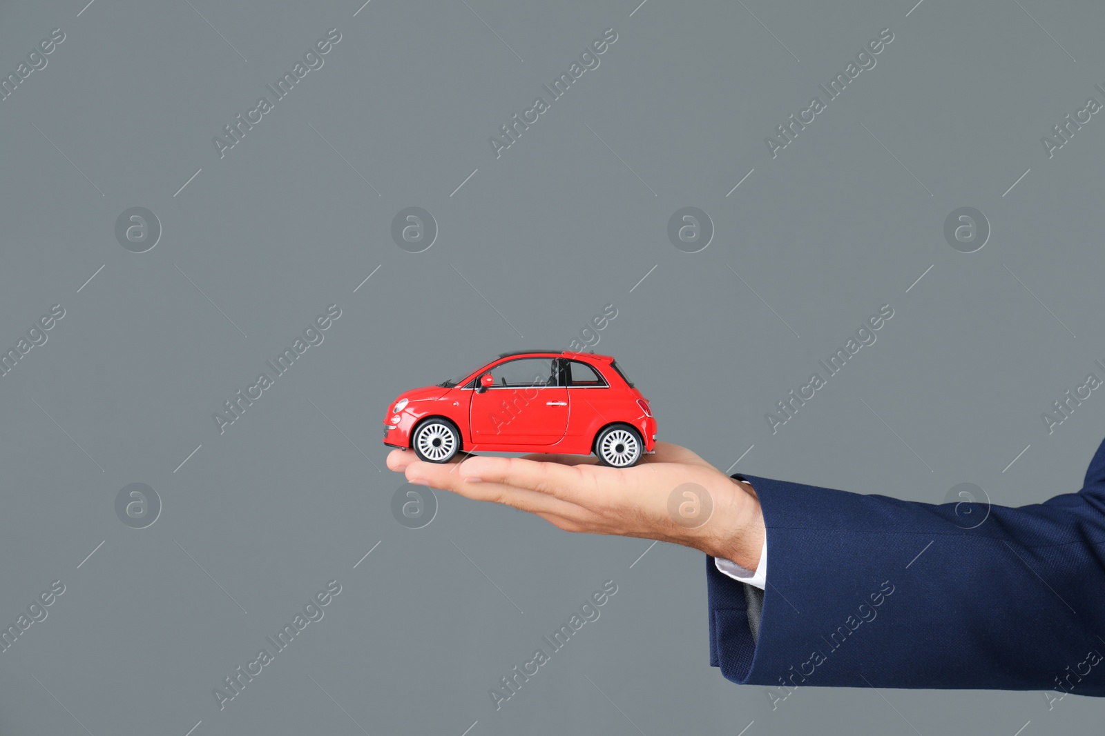 Photo of Insurance agent holding toy car on gray background, closeup