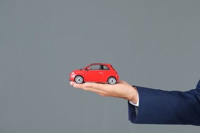 Insurance agent holding toy car on gray background, closeup