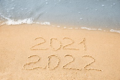 Photo of Dates written on sandy beach. 2021 washed by sea wave as New 2022 Year coming