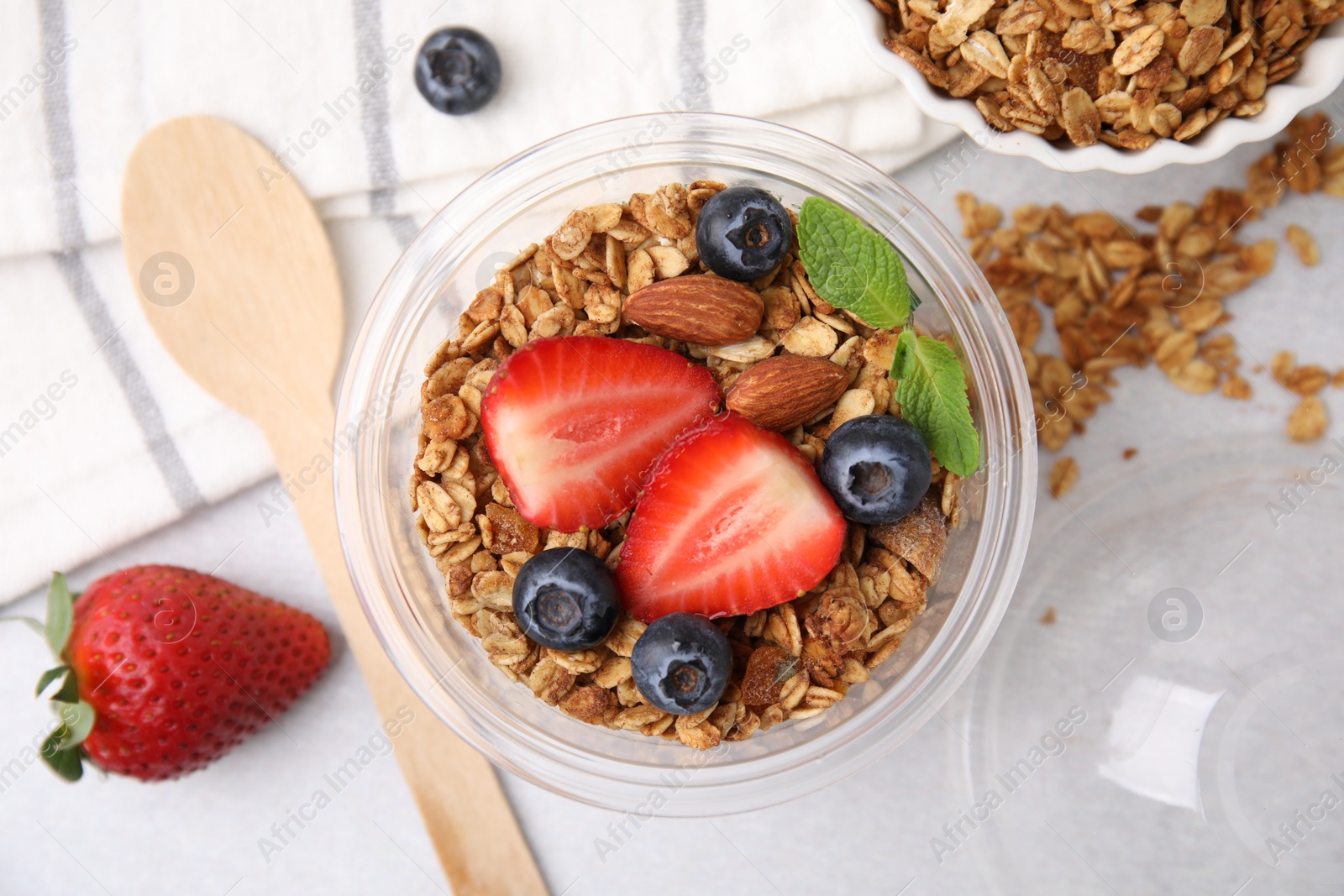 Photo of Tasty granola with berries and nuts in plastic cup on light table, top view