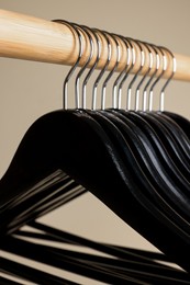 Photo of Black clothes hangers on wooden rail against beige background, closeup