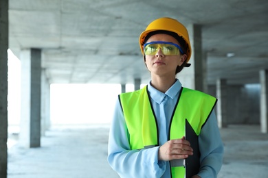 Photo of Professional engineer in safety equipment with clipboard at construction site. Space for text