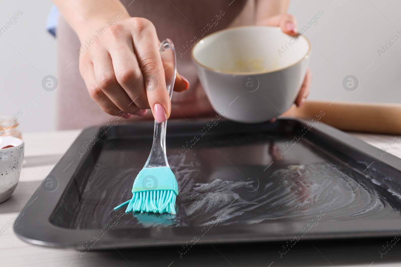 Photo of Making delicious baklava. Woman buttering baking pan at white table, closeup