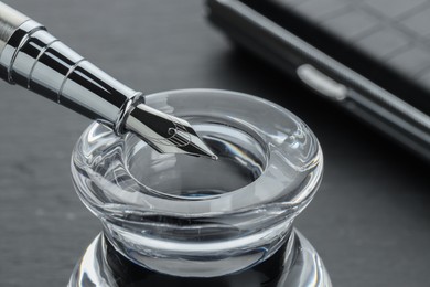 Photo of Inkwell with fountain pen on grey table, closeup