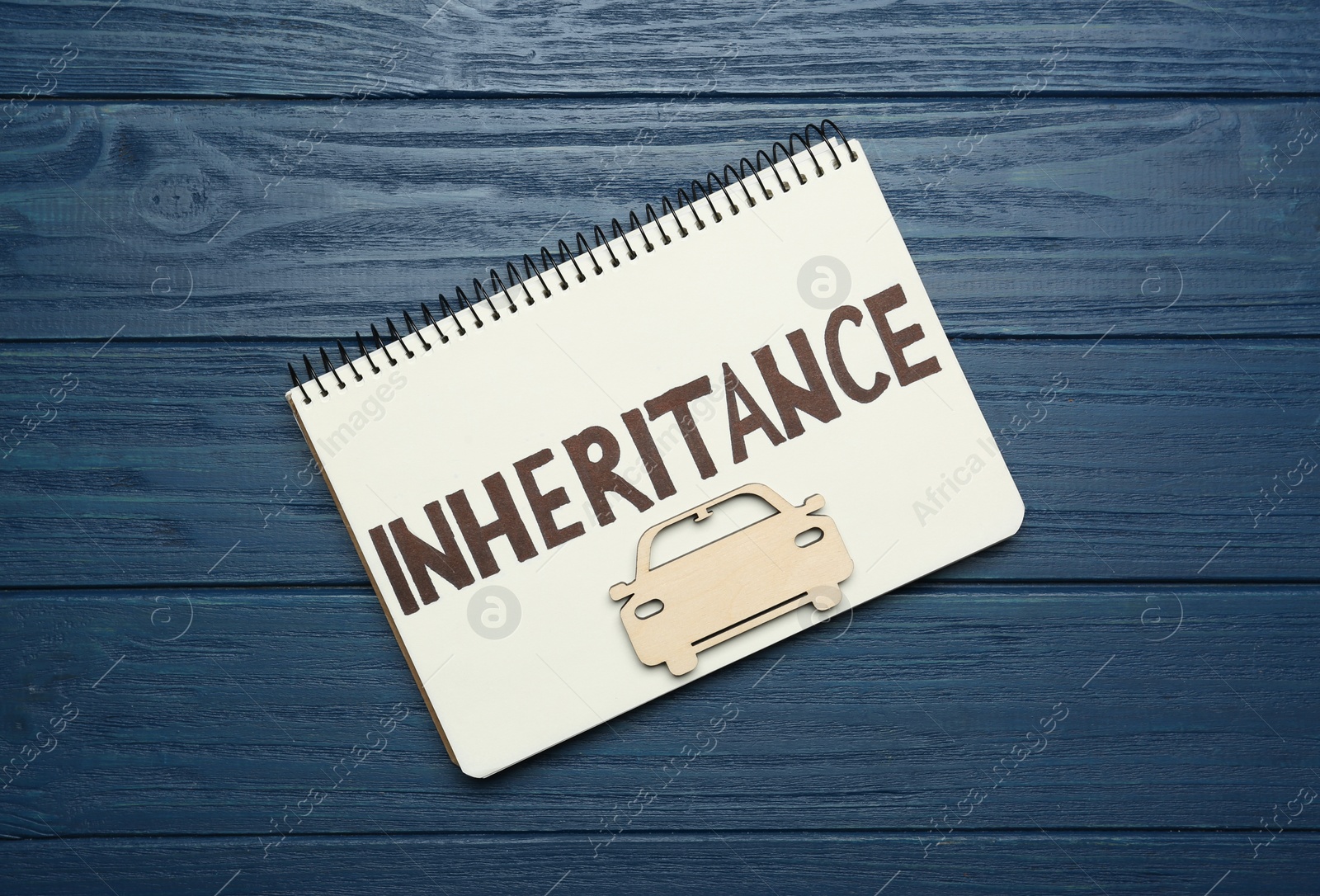 Photo of Notebook with word Inheritance and model of car on blue wooden background, top view