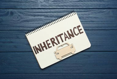 Photo of Notebook with word Inheritance and model of car on blue wooden background, top view