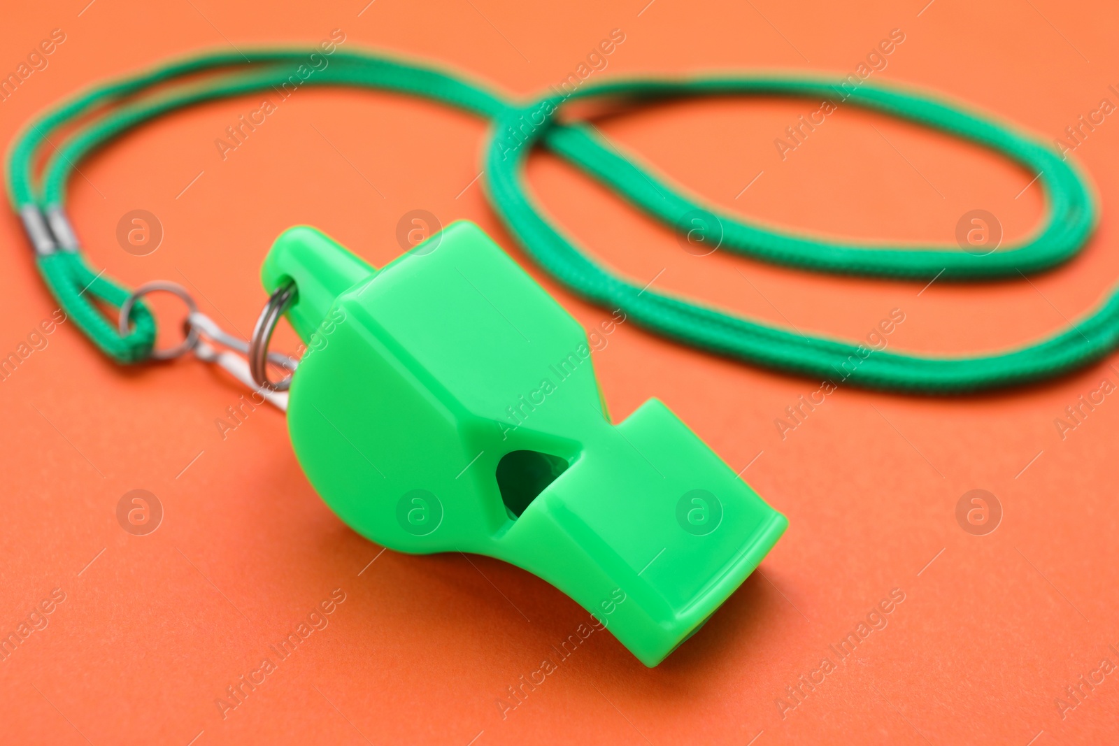 Photo of One green whistle with cord on orange background, closeup