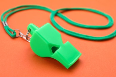 One green whistle with cord on orange background, closeup