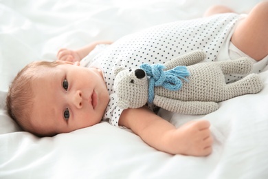 Photo of Adorable newborn baby with toy lying on bed sheet