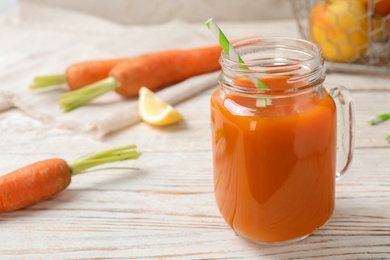 Mason jar with fresh carrot juice on white wooden table, space for text