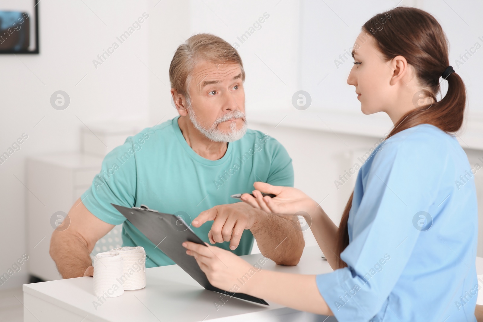 Photo of Professional orthopedist consulting patient at table in clinic