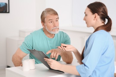 Photo of Professional orthopedist consulting patient at table in clinic