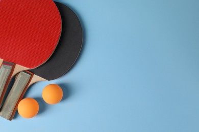 Ping pong balls and rackets on light blue background, flat lay. Space for text