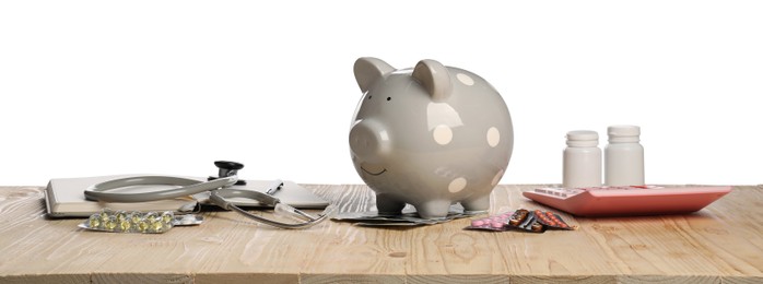 Piggy bank, stethoscope, calculator and pills on wooden table against white background. Medical insurance