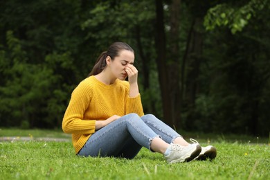 Woman suffering from seasonal spring allergy on green grass in park