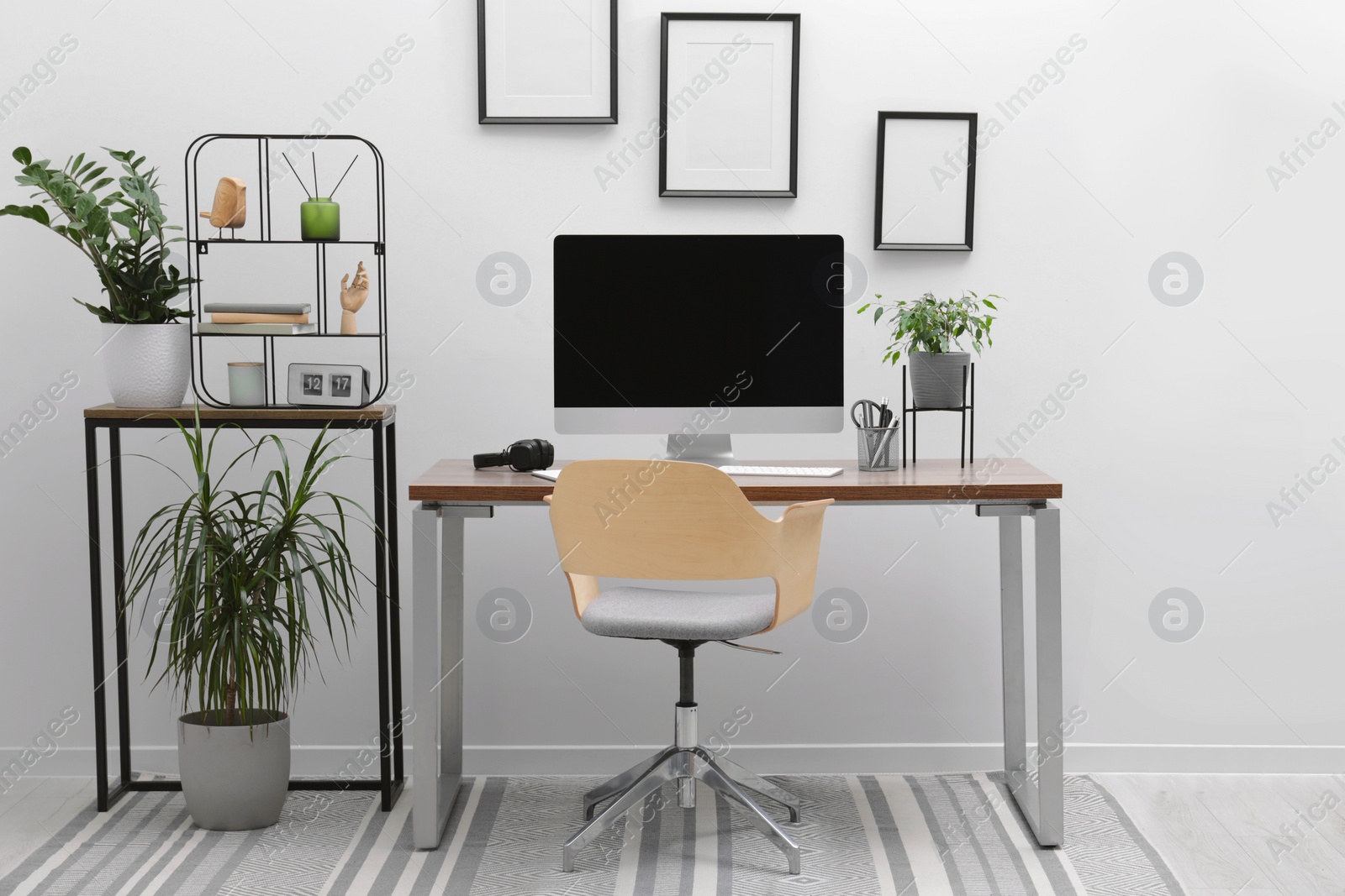 Photo of Cozy workspace with computer on desk, chair and houseplants near white wall at home