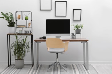 Cozy workspace with computer on desk, chair and houseplants near white wall at home