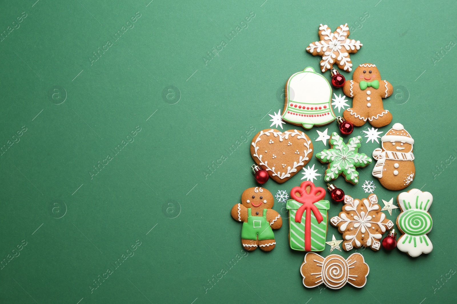 Photo of Christmas tree shape made of delicious gingerbread cookies on green background, flat lay. Space for text