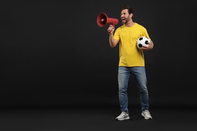 Photo of Emotional sports fan with soccer ball and megaphone on black background, space for text