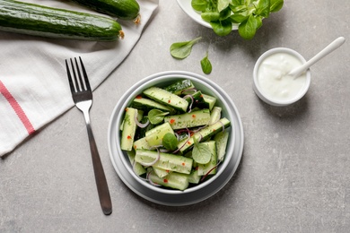 Photo of Delicious cucumber salad with onion and spinach in bowl served on grey table, top view