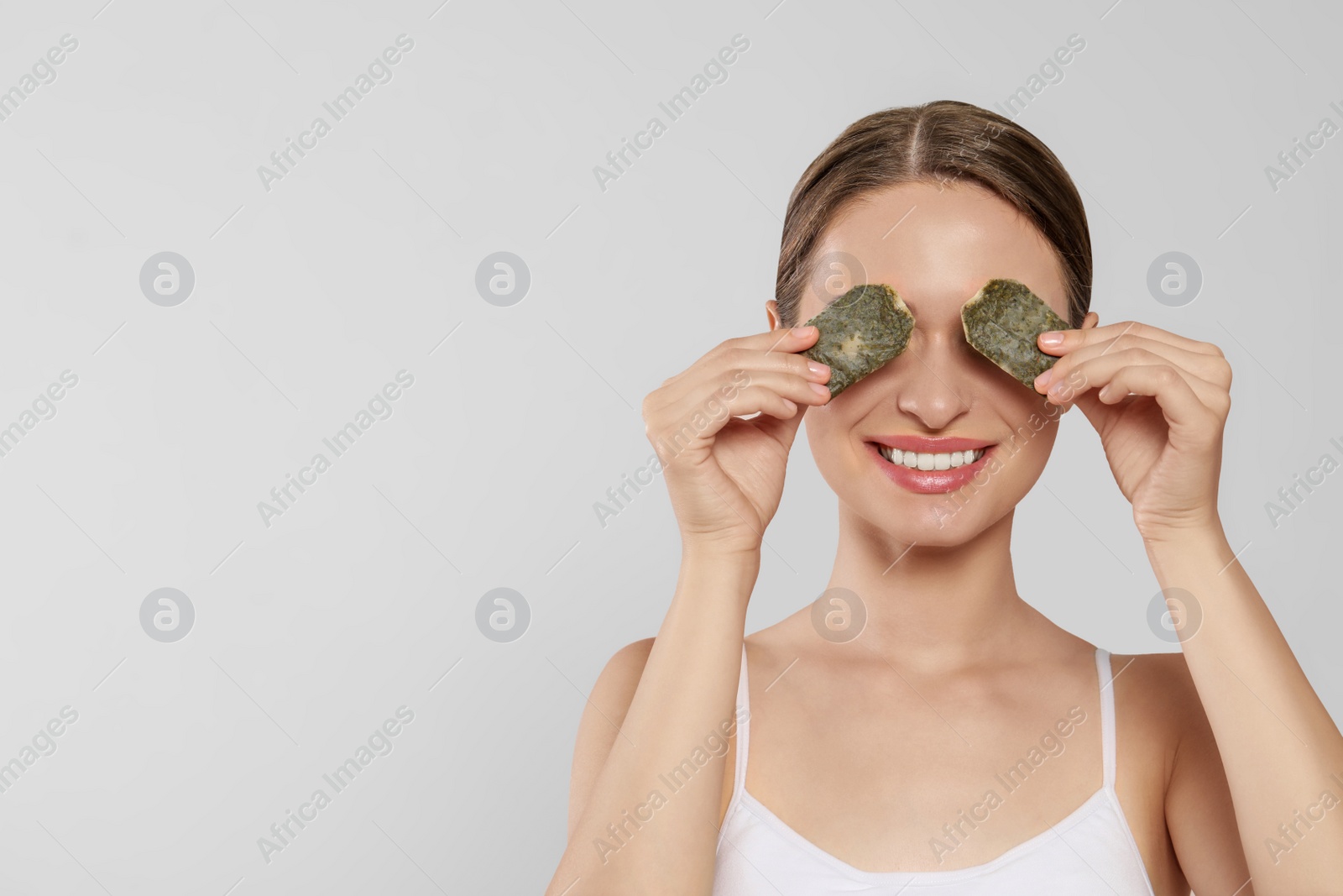 Photo of Young woman with green tea bags on white background. Eye skin care, space for text