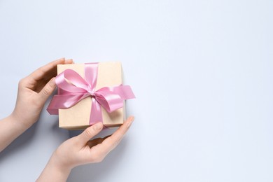 Photo of Woman holding gift box with pink bow on white background, top view. Space for text