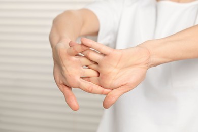 Photo of Woman cracking her knuckles on blurred background, closeup. Bad habit