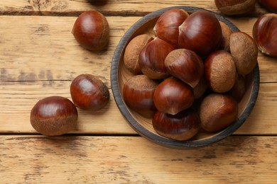 Photo of Sweet fresh edible chestnuts in bowl on wooden table, top view