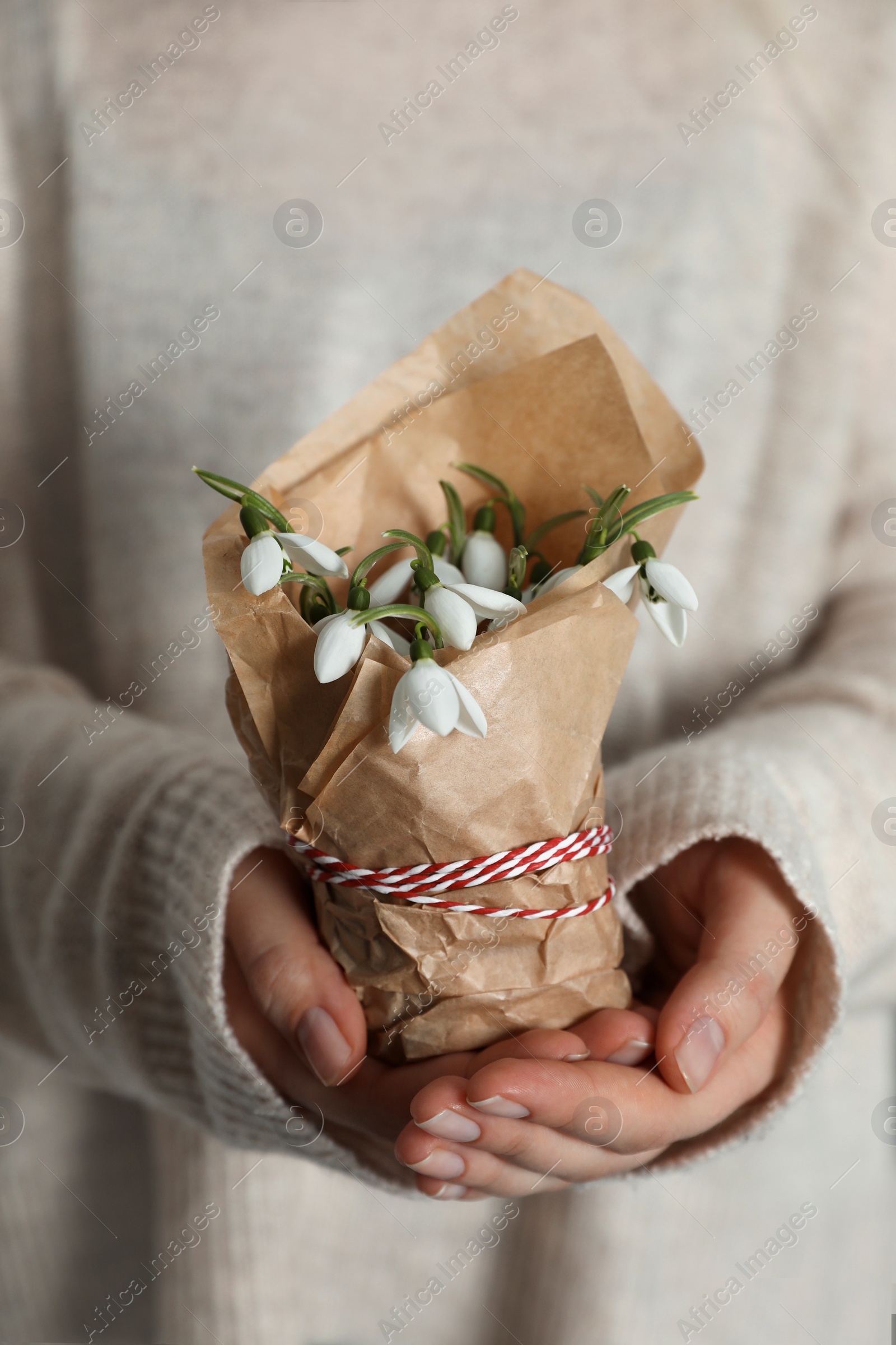 Photo of Woman holding paper bag with beautiful snowdrops and traditional cord martisor, closeup. Symbol of first spring day