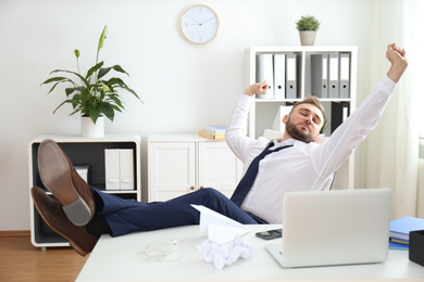 Photo of Lazy young man stretching at table in office