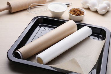 Photo of Baking pan with rolls of parchment paper, different ingredients and kitchen tools on wooden table