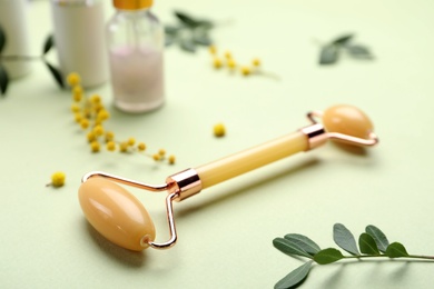 Photo of Natural face roller, cosmetic products and flowers on green background