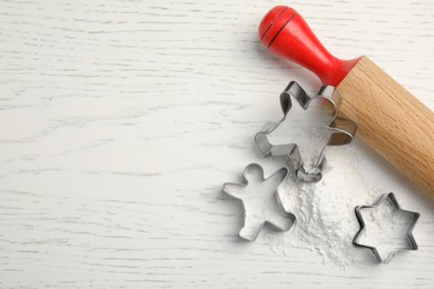 Cookie cutters, rolling pin and flour on white wooden table, flat lay. Space for text