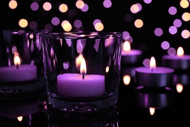 Burning violet candle on black background, closeup. Funeral attributes