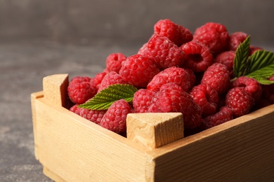 Photo of Wooden crate with delicious ripe raspberries on stone surface, closeup