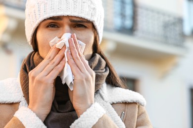 Woman with tissue blowing runny nose outdoors. Cold symptom
