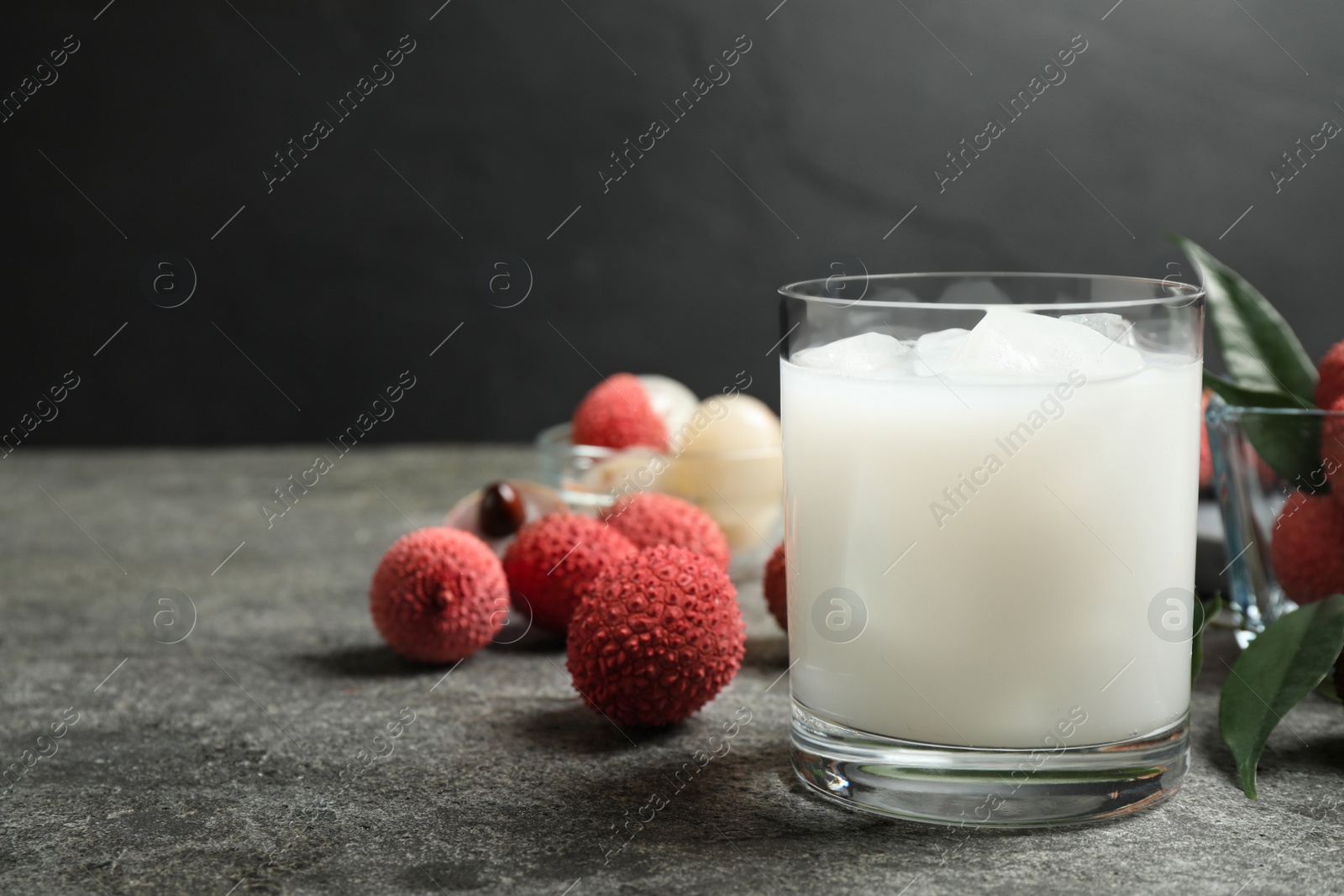 Photo of Lychee juice and fresh fruits on grey table. Space for text