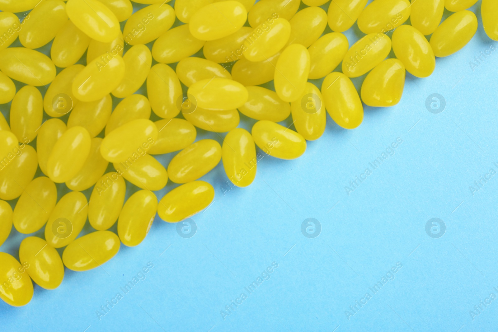 Photo of Many delicious lemon jelly beans on light blue background, flat lay. Space for text