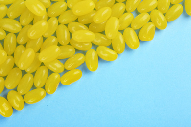 Many delicious lemon jelly beans on light blue background, flat lay. Space for text