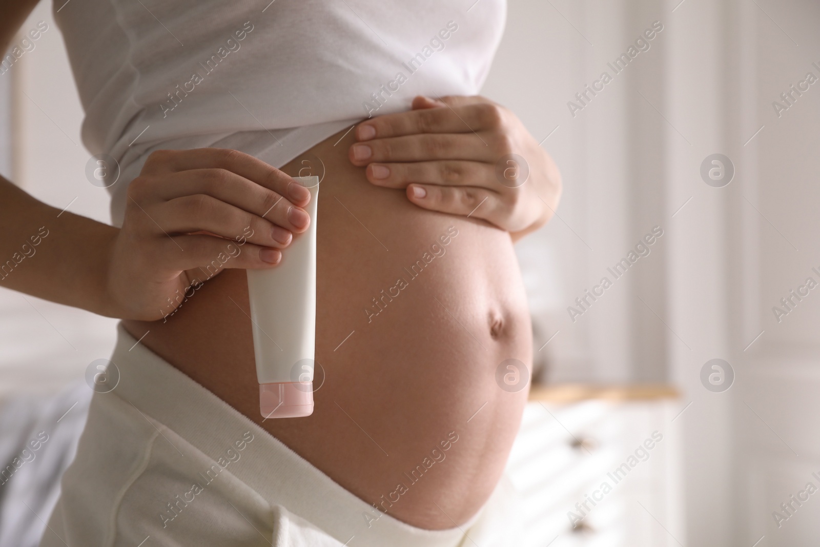 Photo of Young pregnant woman with cosmetic product indoors, closeup. Space for text