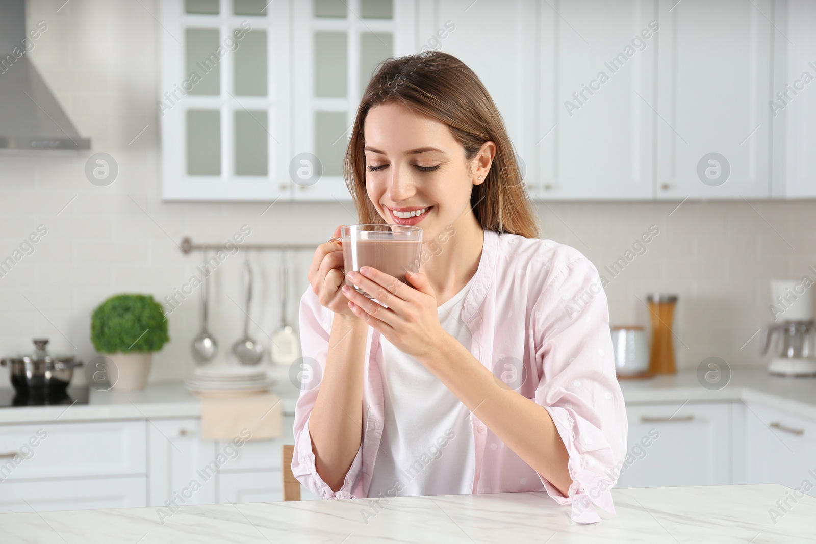 Photo of Young woman drinking chocolate milk in kitchen