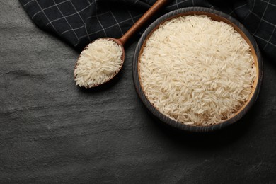 Photo of Raw basmati rice in bowl and spoon on black table, top view. Space for text