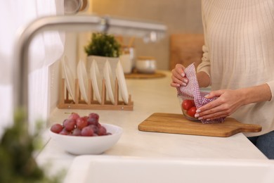 Photo of Woman packing bowl of fresh tomatoes into beeswax food wrap at white countertop in kitchen, closeup