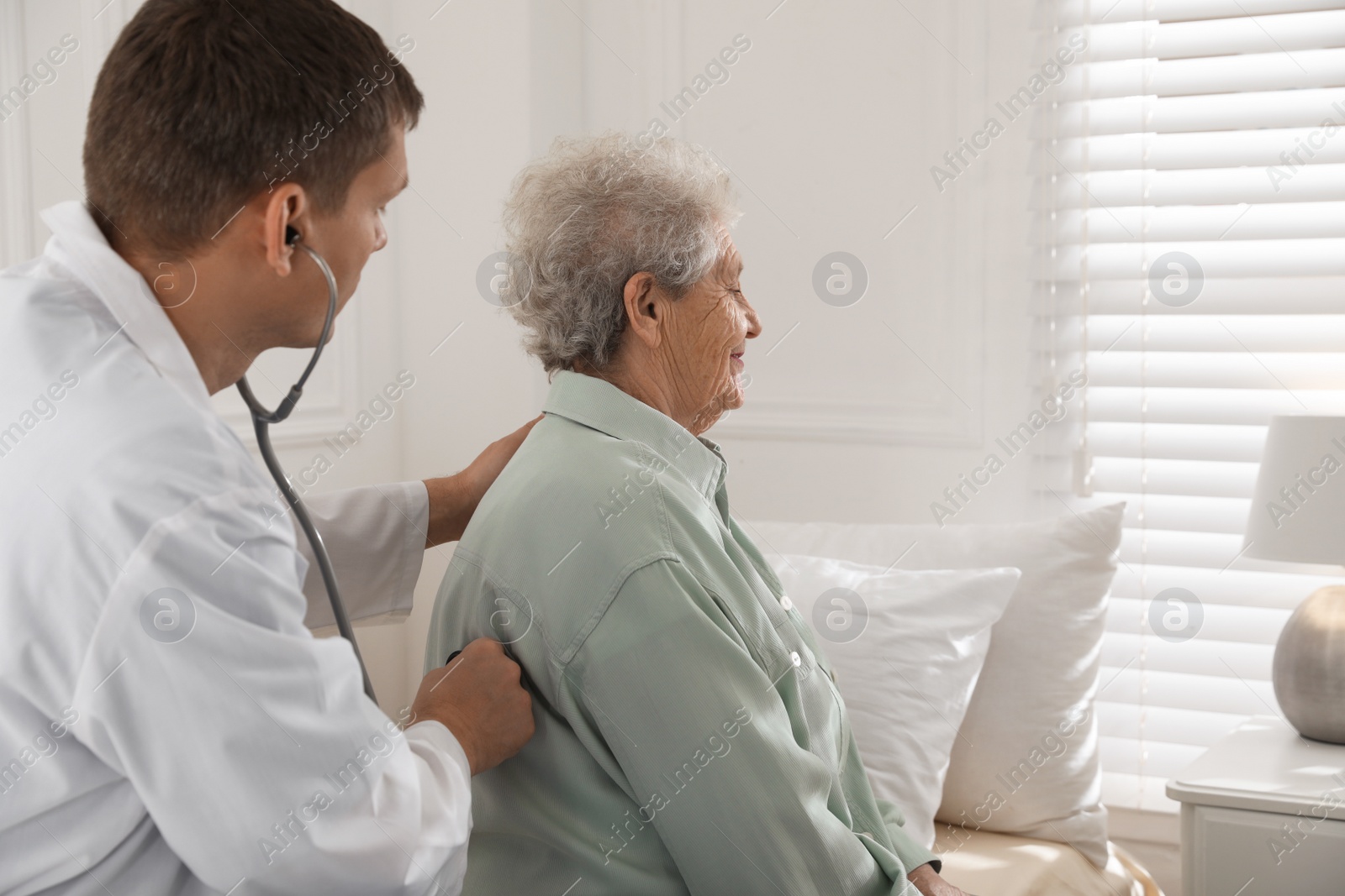 Photo of Caregiver examining senior woman in room. Home health care service