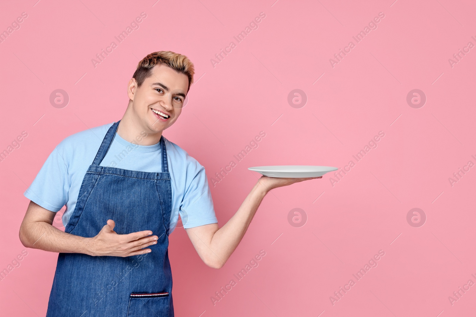 Photo of Portrait of happy confectioner holding empty plate on pink background, space for text