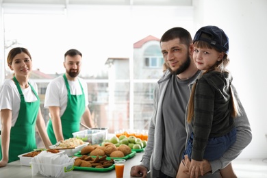 Photo of Poor father and daughter receiving food from volunteers indoors