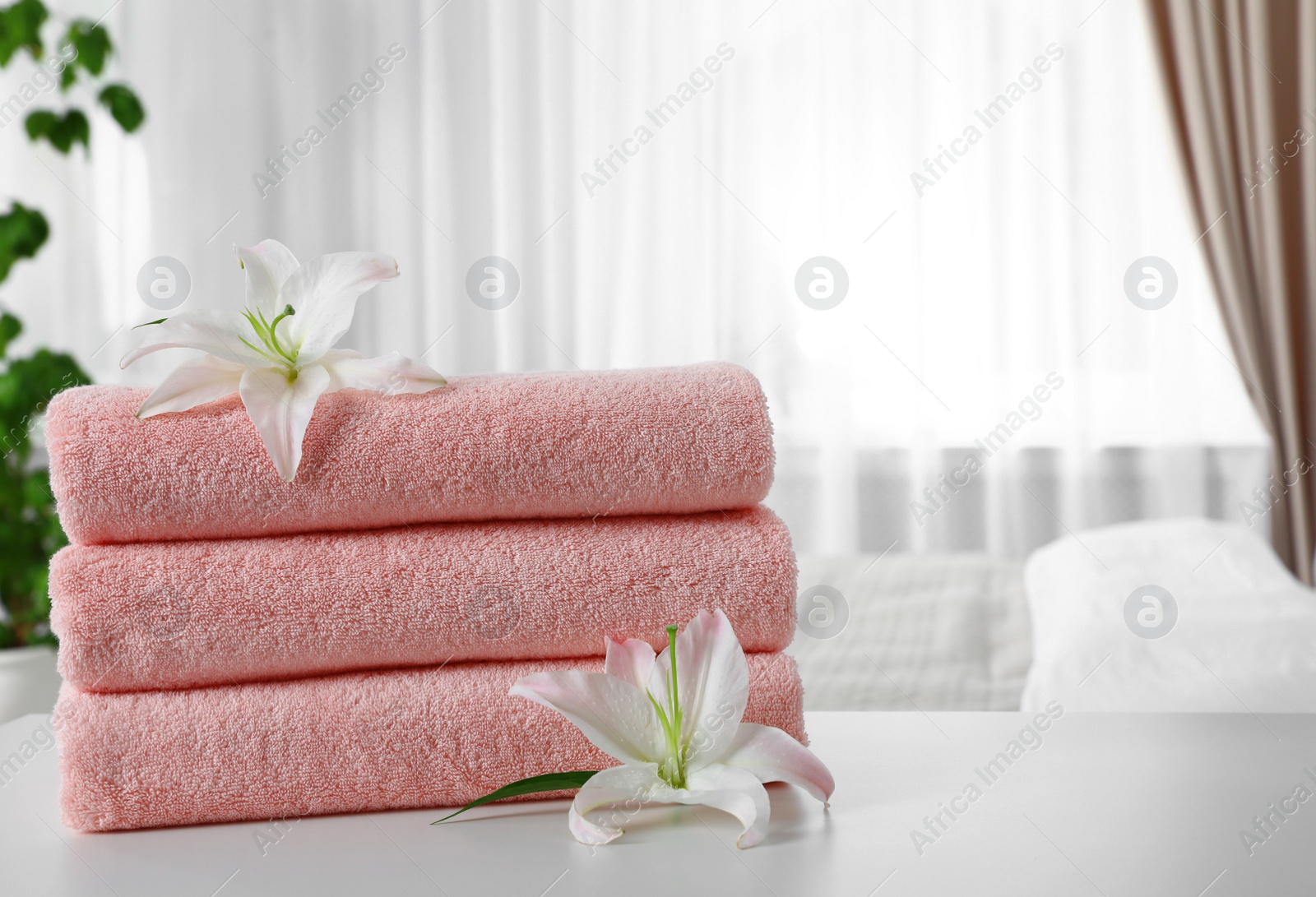 Photo of Stack of fresh towels with flowers on table in bedroom. Space for text